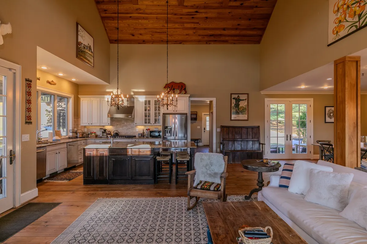 This image showcases a spacious, open-concept kitchen and dining area with a large kitchen island, ample counter space, comfortable seating, a dining table, and high ceilings with exposed wooden beams. Artwork on the walls adds character and warmth.