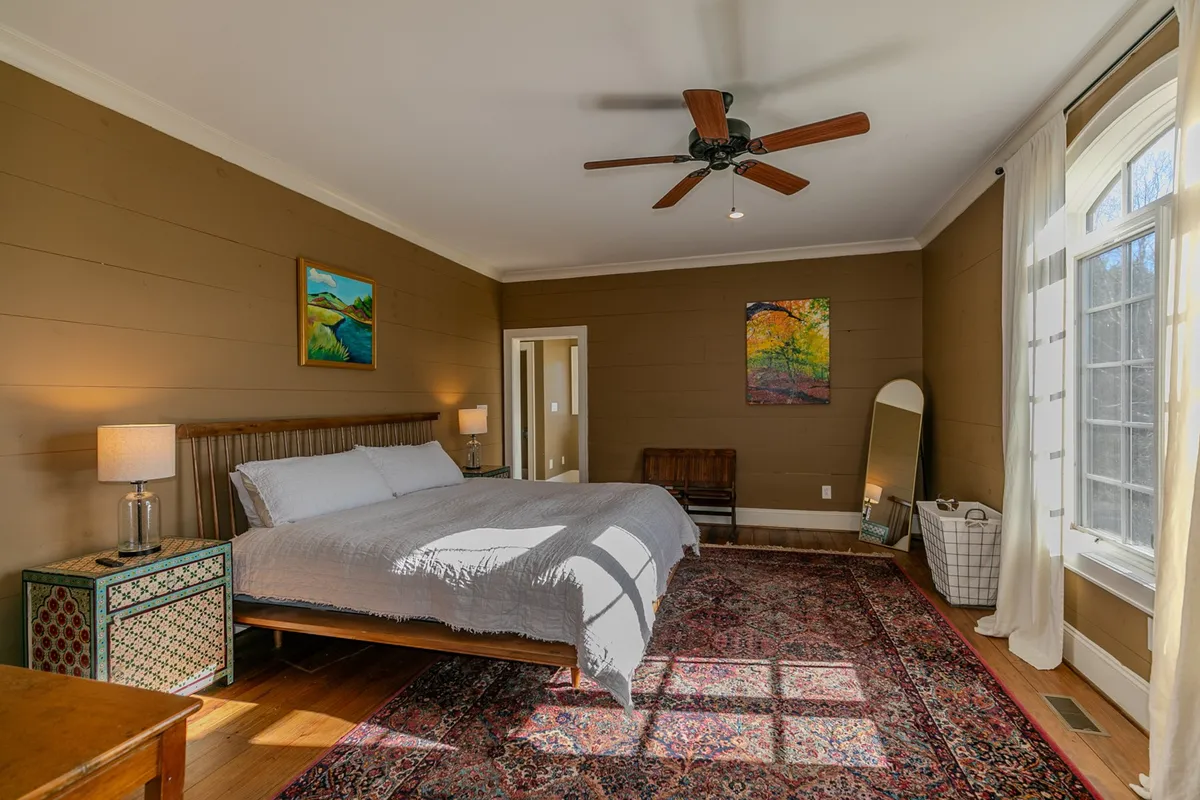 A serene bedroom scene with a comfortable bed, stylish nightstands, soft lighting, a rug, and soothing artwork. Natural light streams in through a window, creating a tranquil and inviting atmosphere.