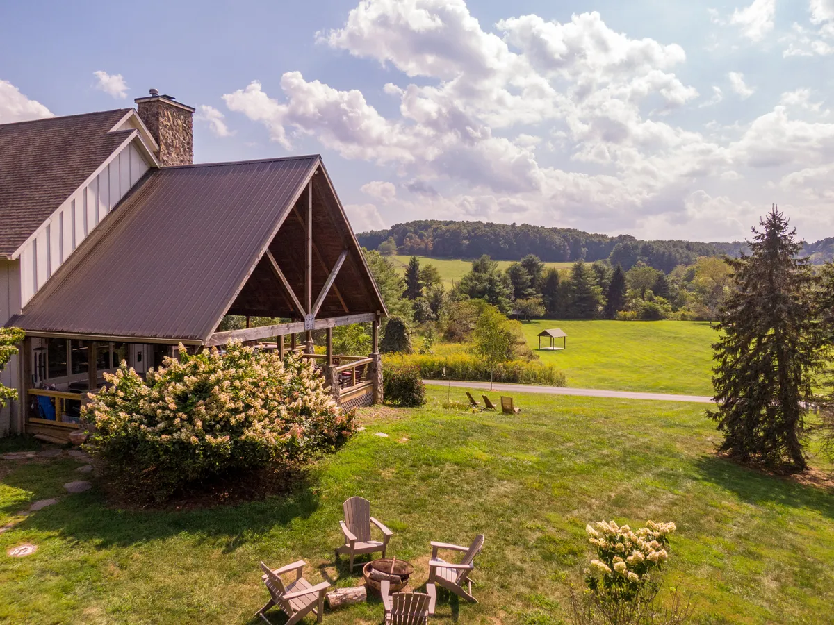 An exterior shot of a large house with an expansive green lawn, a fire pit encircled by chairs, and breathtaking mountain views in the background. The image captures a sense of space and togetherness, ideal for gathering and outdoor activities.