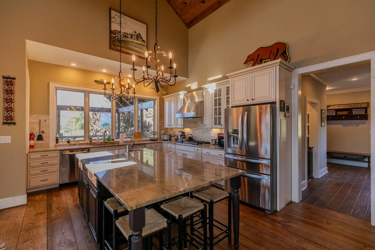 A bright, inviting kitchen featuring a large kitchen island, stainless steel appliances, a striking chandelier, and windows that bathe the space in natural light—ideal for both cooking and socializing.