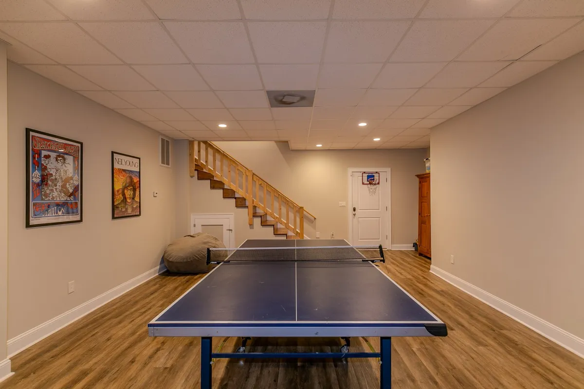 A lively interior game area showcasing a ping pong table, staircase, and art-adorned walls. The space is designed for playful activities, offering a spot for friendly competitions and casual lounging.