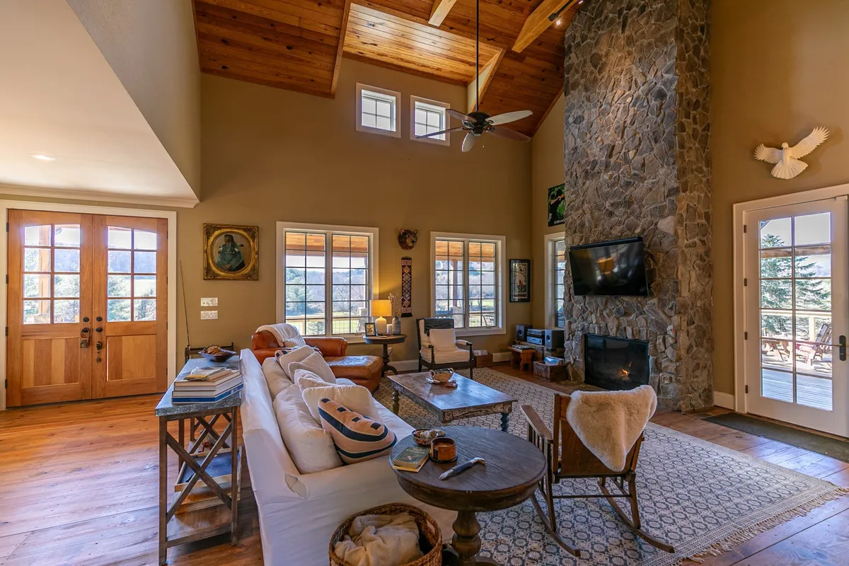 A comfortable seating area with a stone fireplace, exposed wooden beams, and large windows that frame the view outside. The space feels intimate yet open, perfect for relaxing with family or hosting gatherings.