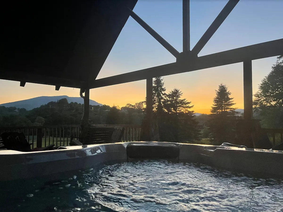 A hot tub positioned on the deck overlooking sweeping mountain vistas and a vibrant sunset sky. The tranquil setting promises relaxation and memorable moments while soaking in warm water with a spectacular view.