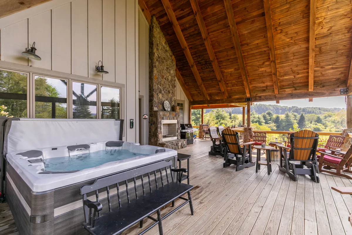 An inviting exterior scene featuring a hot tub, adirondack chairs, a stone fireplace, and panoramic views of the landscape from the porch. The atmosphere is peaceful and rejuvenating, designed for relaxation and socializing while remaining closely connected to the outdoors.